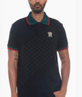A man wearing a black short-sleeve polo shirt with a green collar, red trim, and a subtle repeating monogram pattern across the body. The shirt features a small embroidered crest on the left chest.
