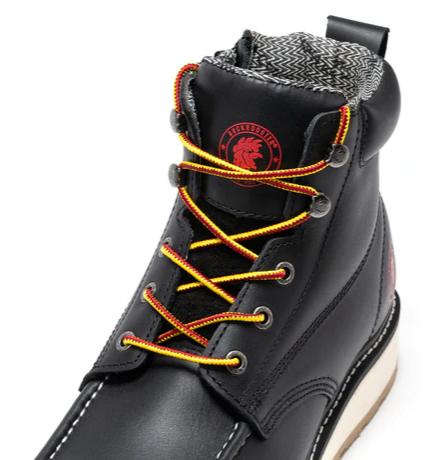 A close-up of a black leather high-top boot with orange and yellow braided laces, a gray patterned lining, and a red circular logo on the tongue.